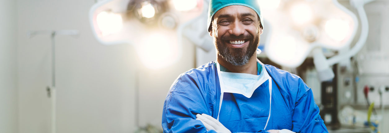 A surgeon stands and smiles in a hospital surgery center.